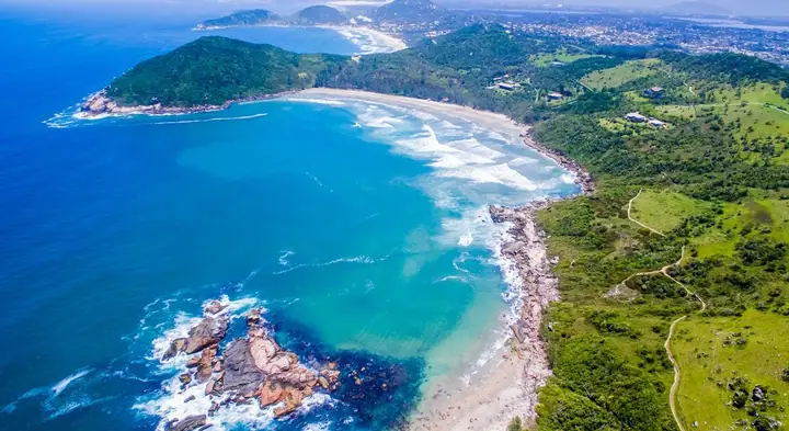 Vista aérea de enseada com praia de areia clara, pedras e morros cobertos de vegetação