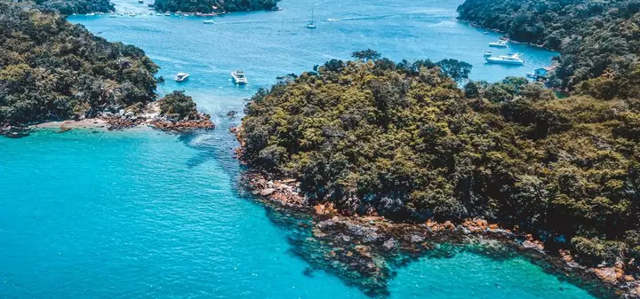 Vista aérea de ilhas cobertas de mata separadas por canal de água turquesa, com lanchas