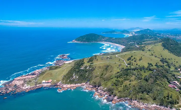 Vista aérea de península coberta de vegetação, com costão rochoso, praias e mar azul