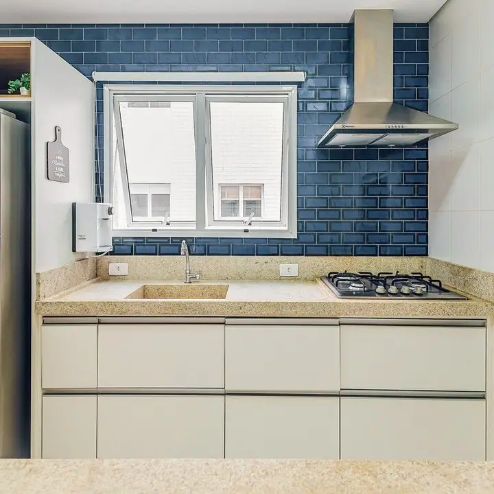 Cozinha com azulejos azuis tipo metrô, coifa de inox, geladeira e armários claros