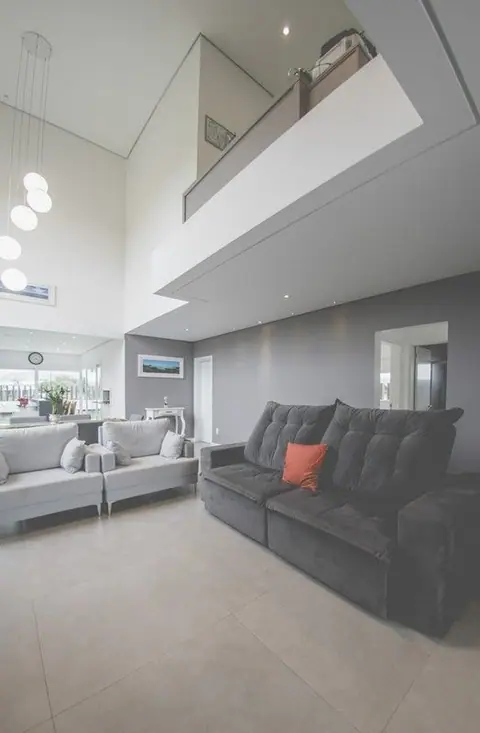 Sala com sofá cinza sob o mezanino de vidro, pendentes de vidro e pé-direito duplo em casa contemporânea
