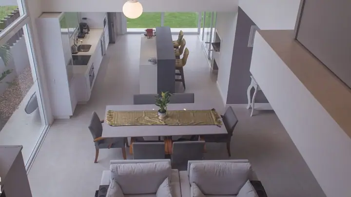 Vista do alto da sala de jantar e da cozinha integradas em casa contemporânea, com mesa posta e poltronas cinza