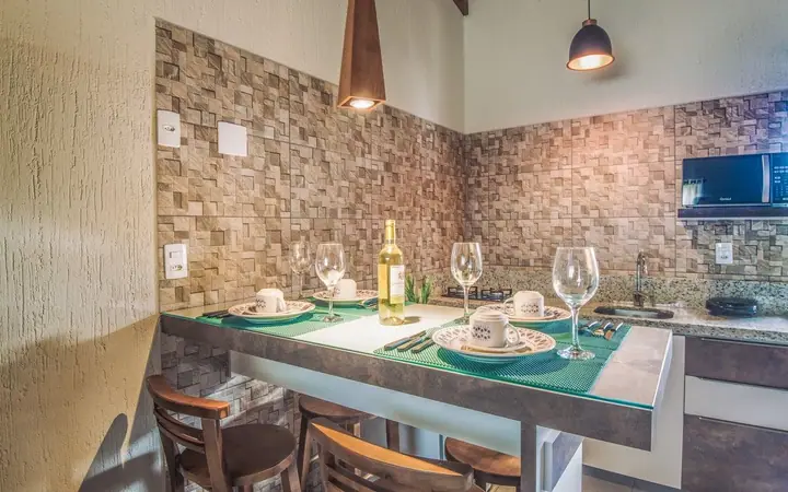 Cozinha compacta de chalé com mesa posta para dois, taças, vinho, parede de pedra e pendentes