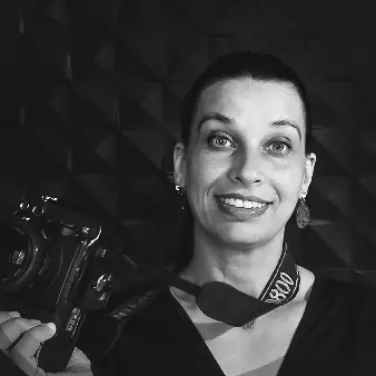 Patricia Picetti sorrindo, com a câmera fotográfica nas mãos, em retrato em preto e branco