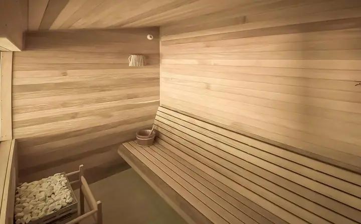 Sauna seca revestida em madeira clara, com bancos em níveis e balde de madeira